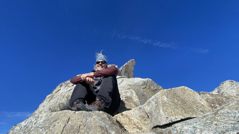 Joe Knauer sitzt auf einem Felsen unter blauem Himmel
